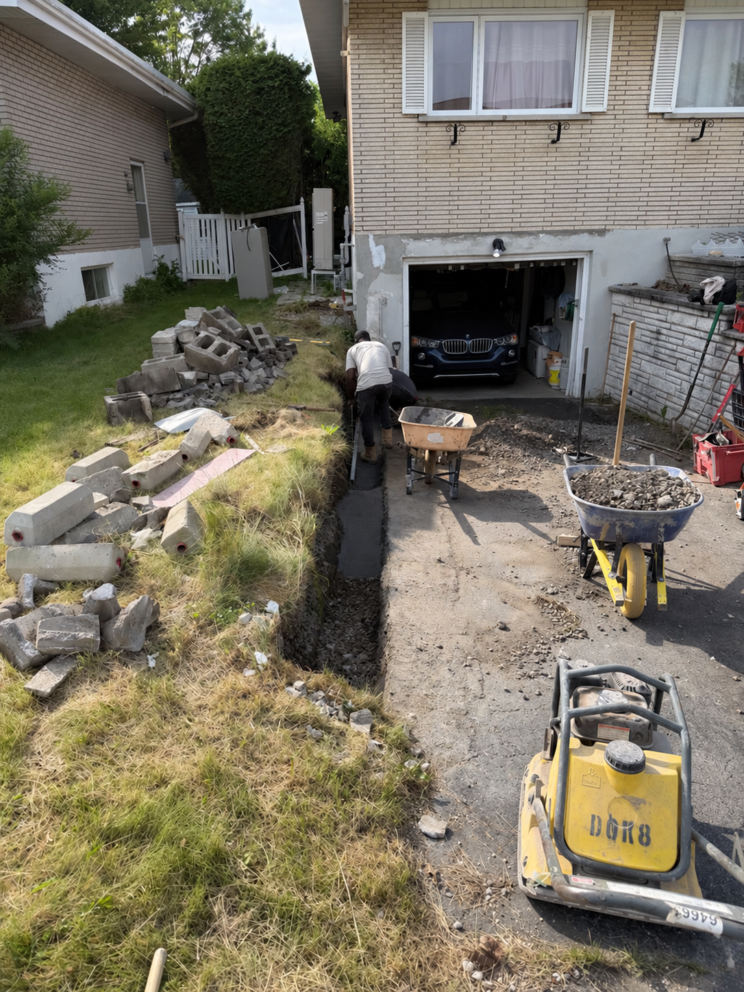 Plaque vibrante au premier plan d’un chantier d’aménagement près d’un garage